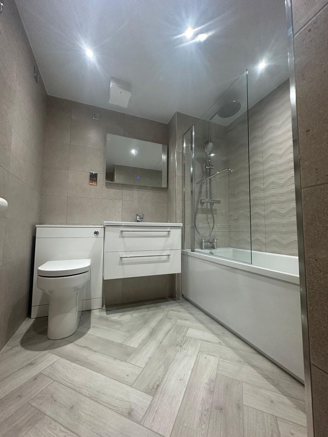Completed bathroom with a bath, glass screen, textured feature tiling and herringbone flooring