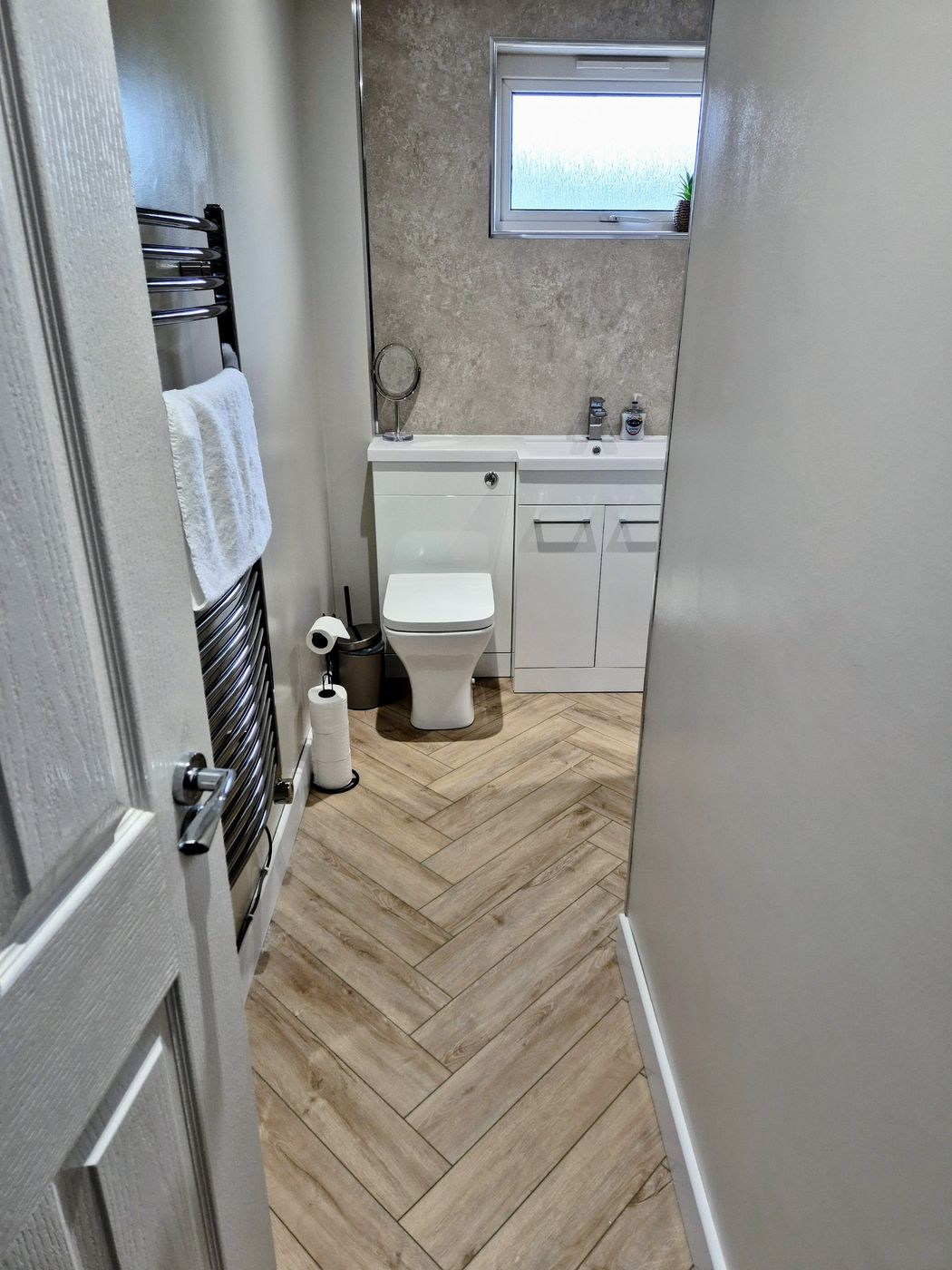 Compact cloakroom with a combined toilet and basin unit, herringbone flooring and a heated towel rail